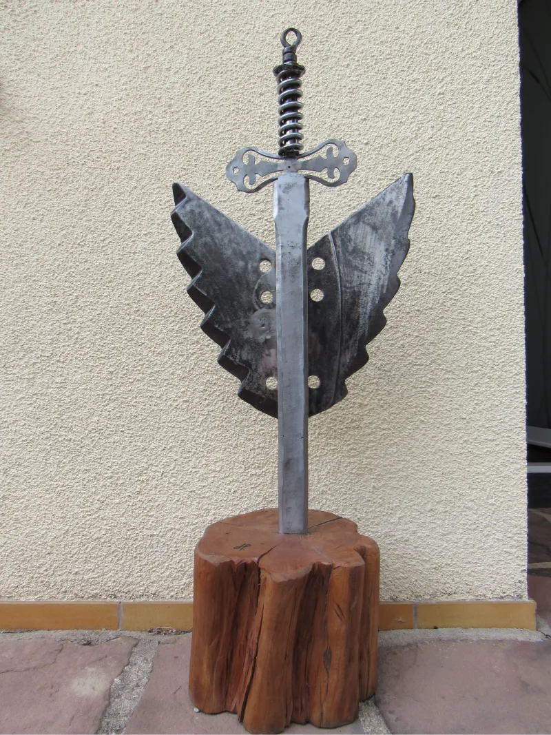 Sculpture métallique représentant une épeé avec des ailes plantée dans un bloc de bois réalisé par Jérôme PETELOT
